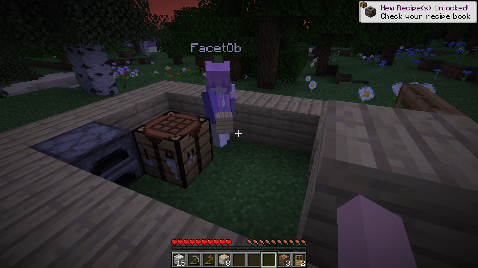 Alice steht zusammen mit einer Werkbank und einem Ofen in einem kleinen, hüfthohen Kasten aus Birkenholzbrettern. Auf dessen rechter Seite befindet sich bereits eine Eingangstür. Viele verschiedene Blumen stehen in der Umgebung.