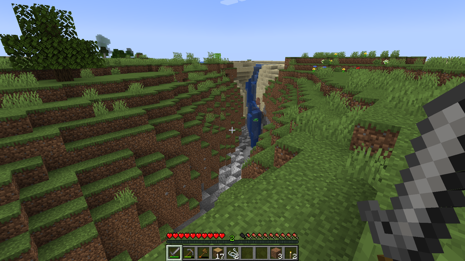 Blick in eine Erdspalte, dessen hinteres Ende in einen Sandstrand schneidet. Meerwasser dringt ein und eine Schildkröte schwimmt in dem resultierenden Wasserfall.